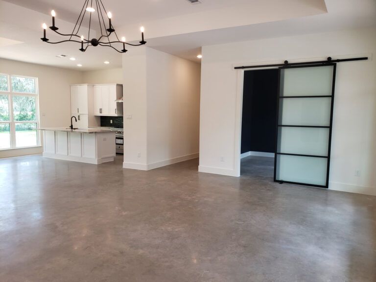 Open-concept living space with polished concrete floors, white walls, and a black sliding door.