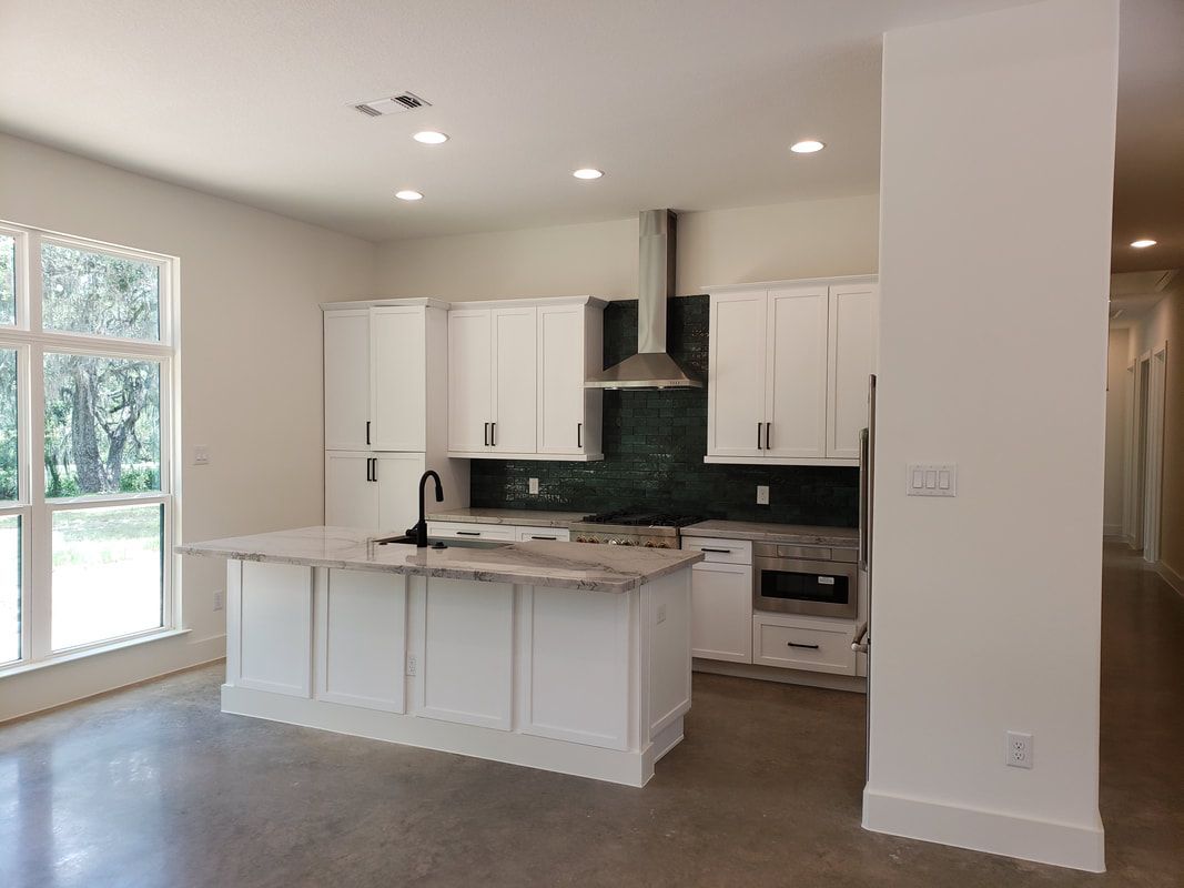 White kitchen with island, cabinets, stainless steel range hood, and large window.