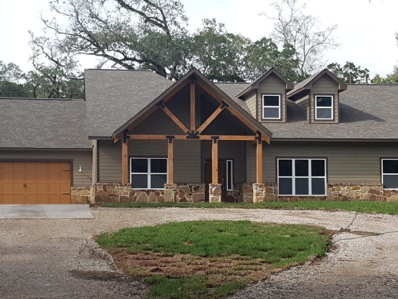 Green house with brown trim and stone accents. Features a covered porch and garage.