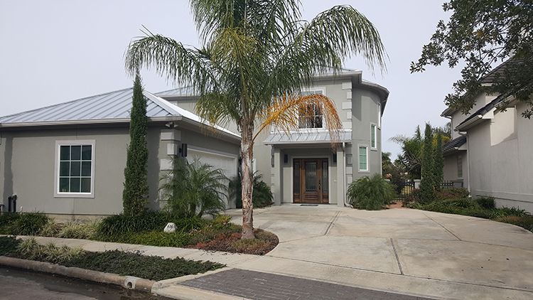 Two-story house with curved facade, light gray stucco exterior, palm tree, and a concrete driveway.