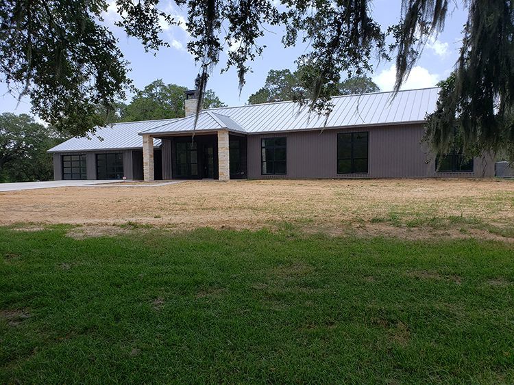 Modern single-story house with gray siding, metal roof, and large windows on a grassy lawn.