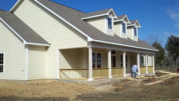 Beige house with porch and three dormers under construction; person on porch.