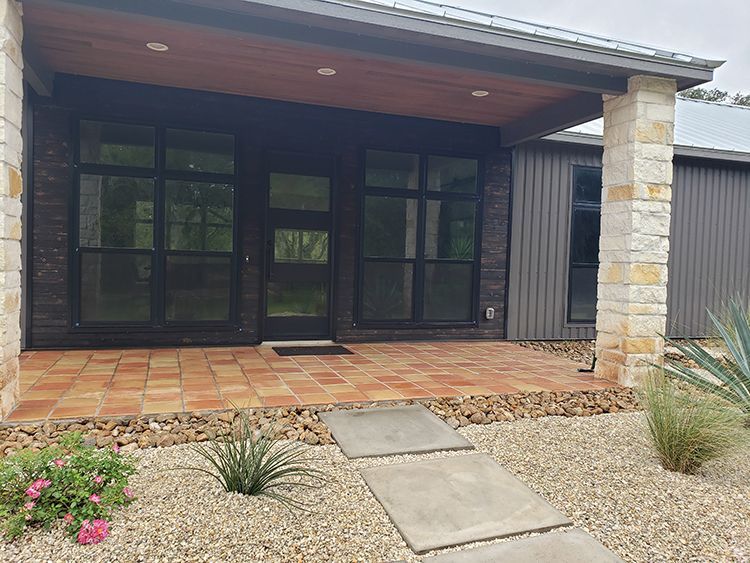 Front exterior of a modern home with stone columns, dark windows, and a terracotta-tiled porch.