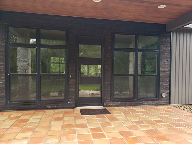 Exterior view of a building with large windows and a terracotta-tiled patio. Dark brown trim and a wooden roof.