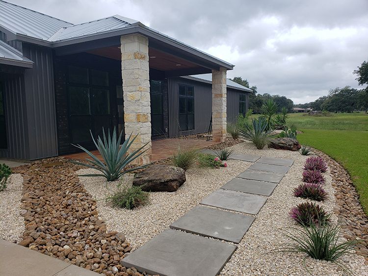 Gray house with stone columns, pathway, and landscaped yard.