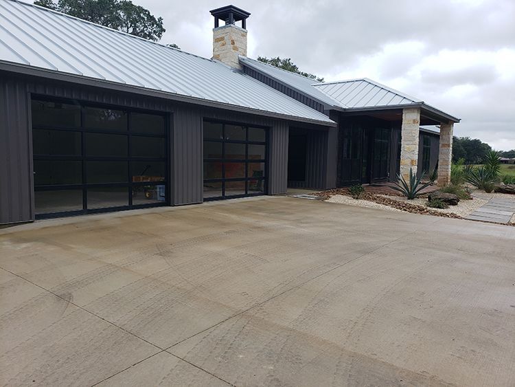 Modern house with gray exterior, metal roof, glass garage doors, and concrete driveway.