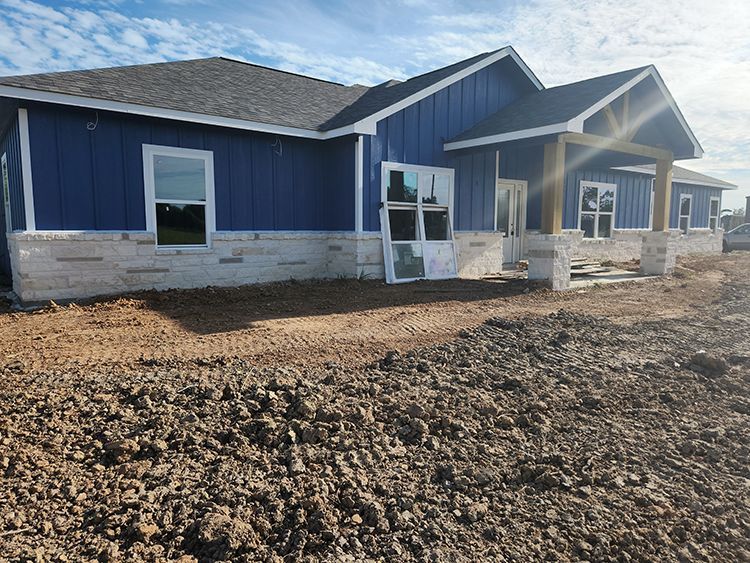 Blue and stone exterior of a house under construction; dirt in front.