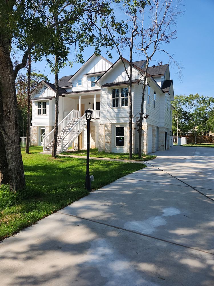 White two-story house with stone accents, stairs, and a concrete driveway. Trees frame the property.