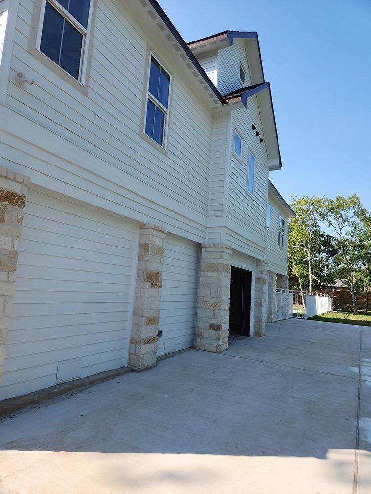 Two-story white house with garage, stone pillars, blue sky, and a concrete driveway.