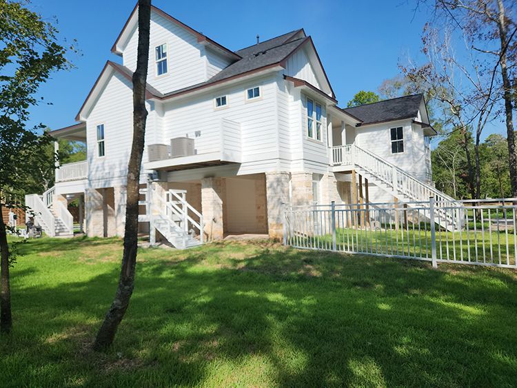 White two-story house on elevated foundation with a stone base, white railings, and a green lawn.