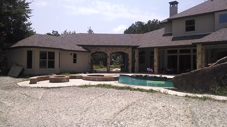 Backyard of a house with a concrete patio, fire pits, and a pool.