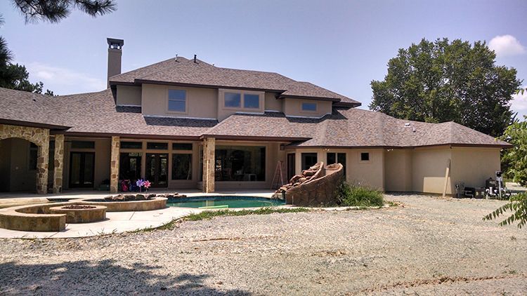 Large beige house with a pool, patio, and stone fire pit on a gravel lot.