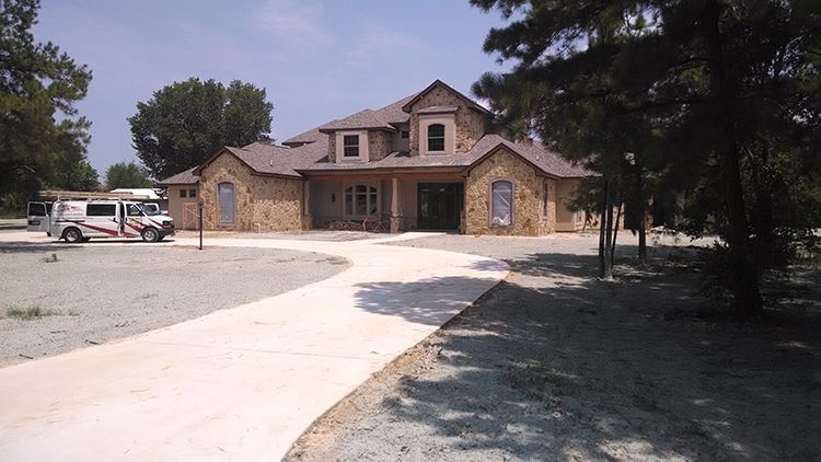 Stone house with curved concrete driveway, RV parked nearby, sunny day.