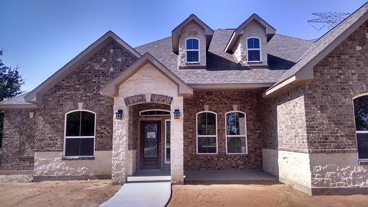 Brick house with stone accents, arched windows, and dormers under a blue sky.