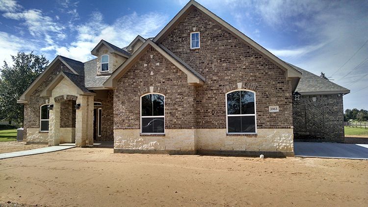 Brick house with light beige trim, two-story, two arched windows, and a bare front yard.