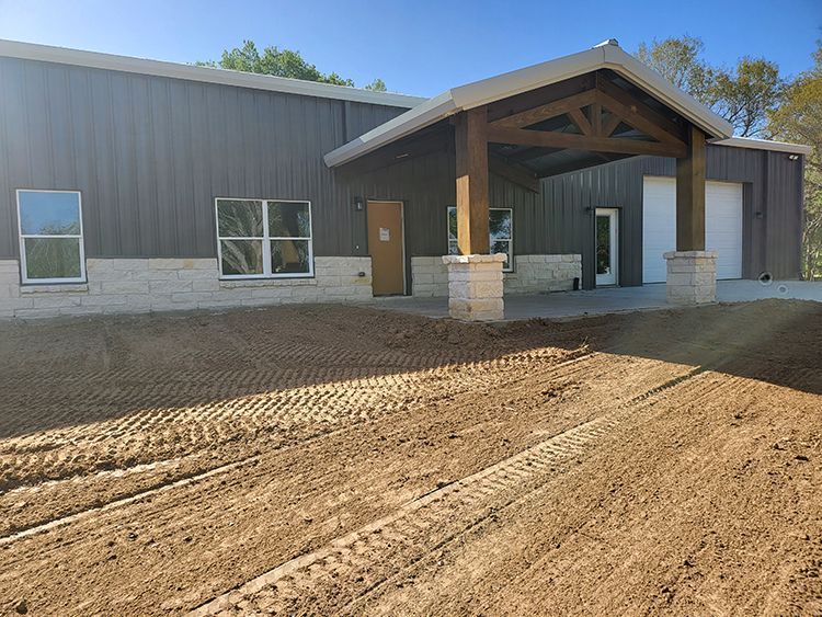 A metal building with a wooden porch and a gravel driveway under a blue sky.