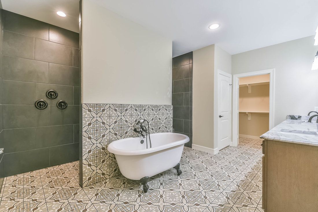 Bathroom with a claw-foot tub, patterned tile floor, walk-in shower, and a vanity, with a walk-in closet in the background.