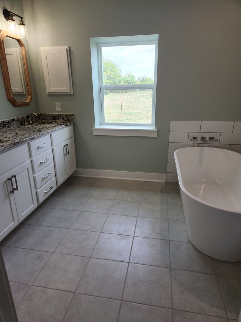 Bathroom with a white freestanding tub, white vanity, and gray tile floor.