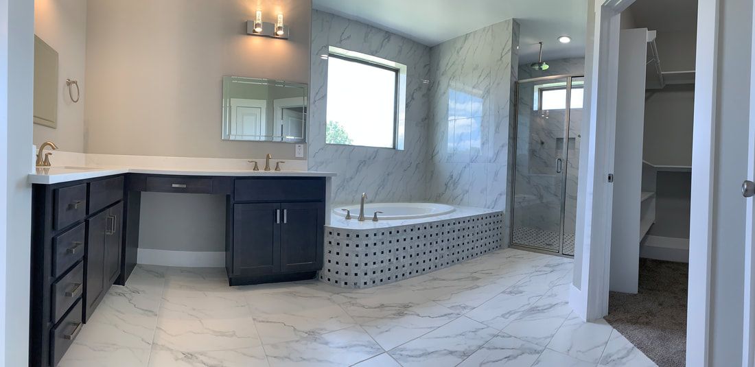 A modern bathroom with marble floors and walls, a soaking tub, and dark gray cabinets.