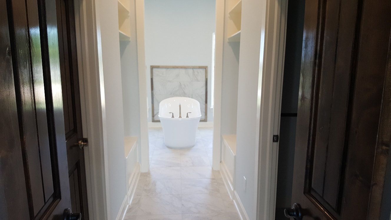 Hallway leading to a white bathtub, flanked by built-in shelves.