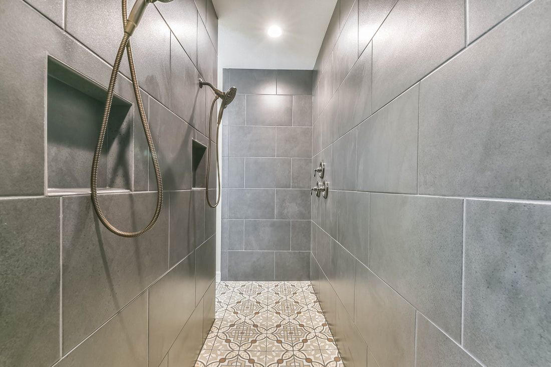 Gray tiled shower with pebble floor, built-in shelf, and rain showerhead.