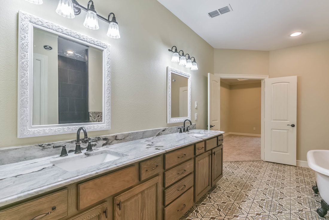 Bathroom with double vanity, mirrors, and a walk-in closet, with beige walls and patterned floor.