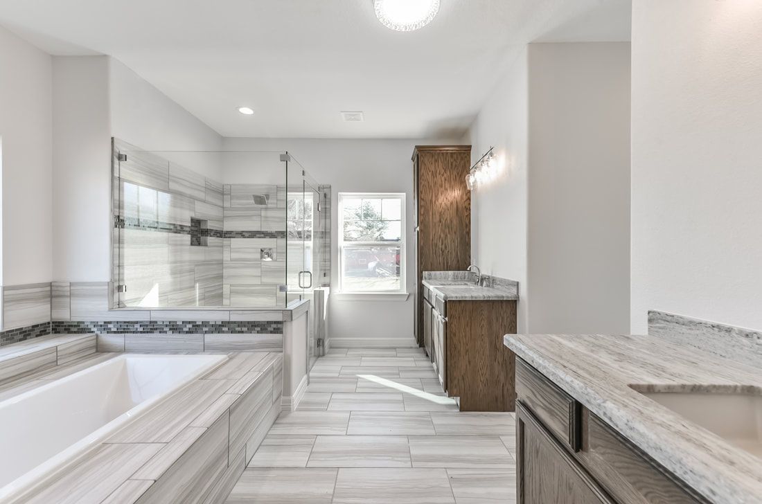 Spacious modern bathroom with a tub, glass shower, double vanity, and light wood cabinetry; light gray and white.
