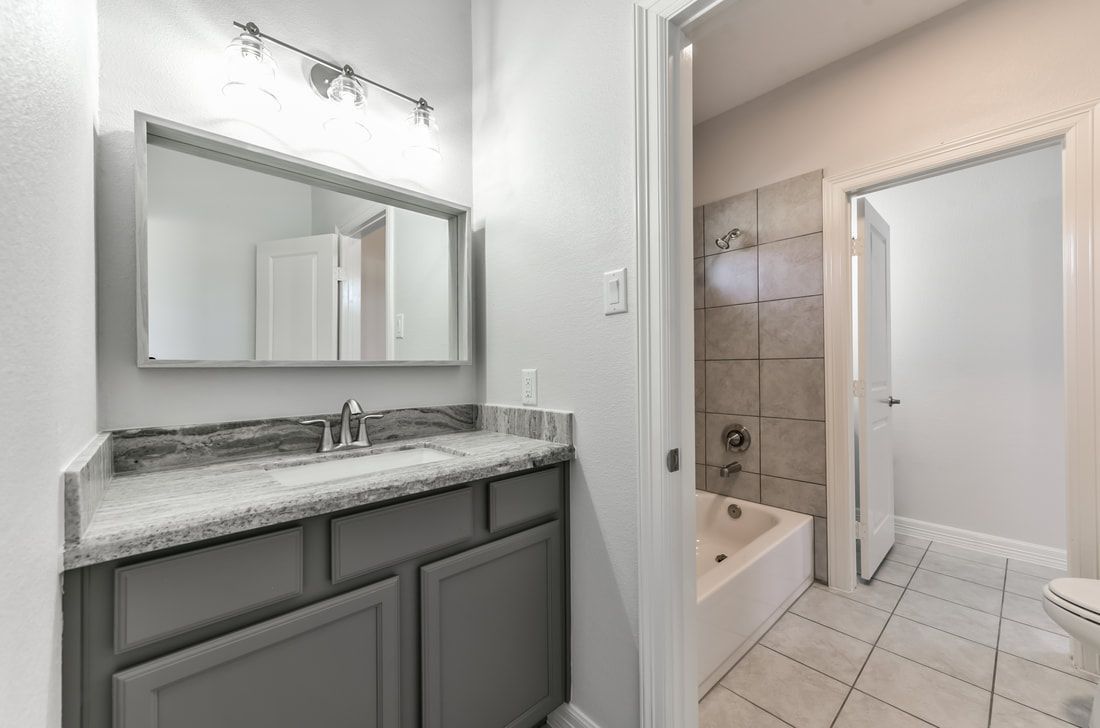 Bathroom with gray vanity, mirror, tub, and doorway. White walls and tile.