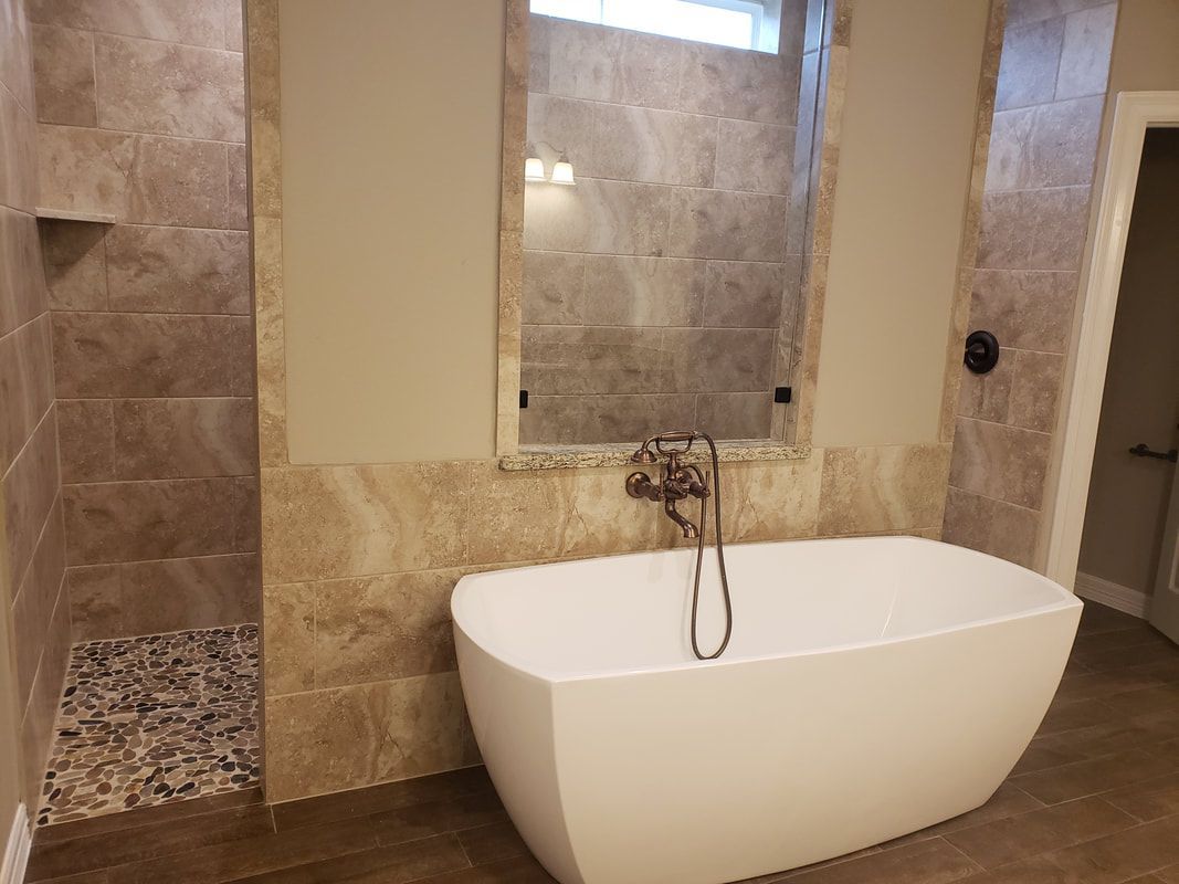 Bathroom with a white freestanding tub, stone tile walls, and a shower with pebble floor.