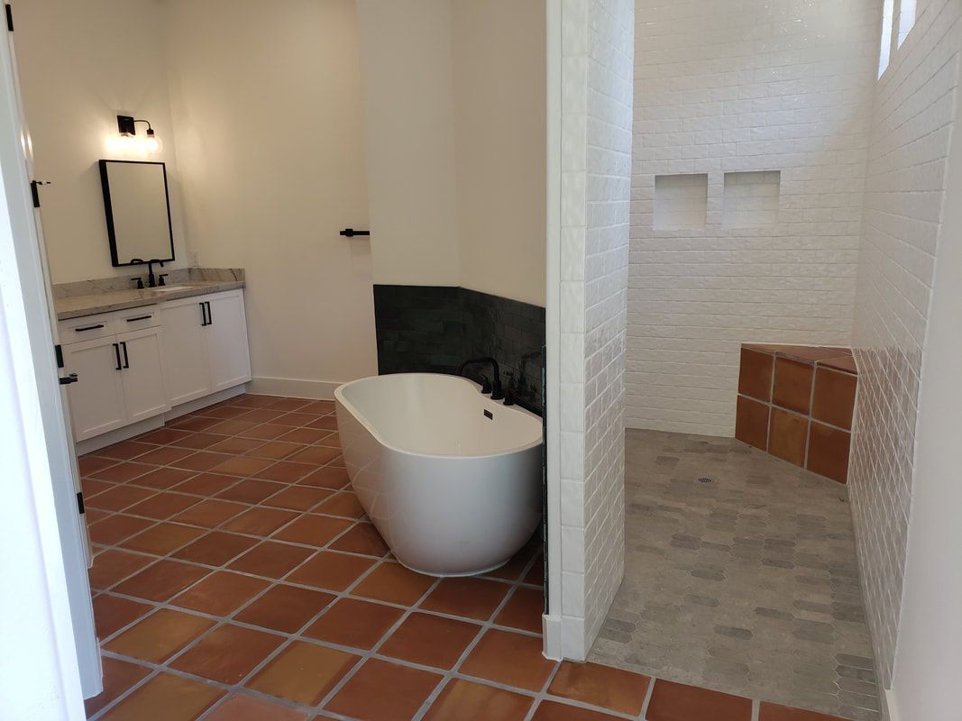 Bathroom with terracotta tile floor, white tub, and tiled shower with built-in bench.