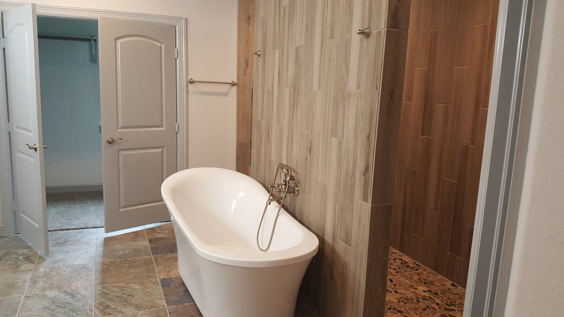 Bathroom with a freestanding white tub, wood-look tiled shower, and light-colored flooring.