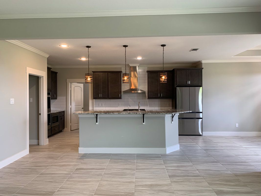 Open kitchen with island, brown cabinets, stainless steel appliances, and pendant lights.
