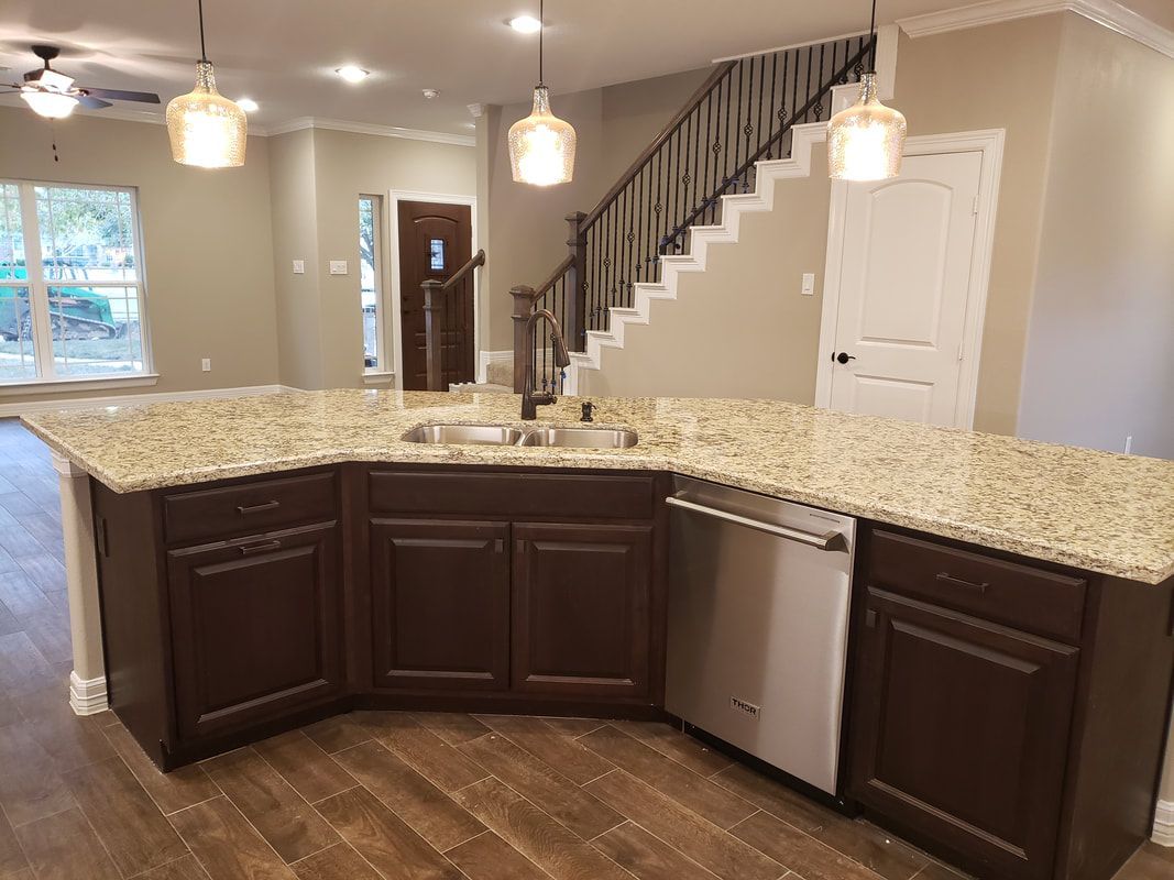 Kitchen with brown cabinets, granite countertops, and stainless steel dishwasher. Staircase and hanging lights.