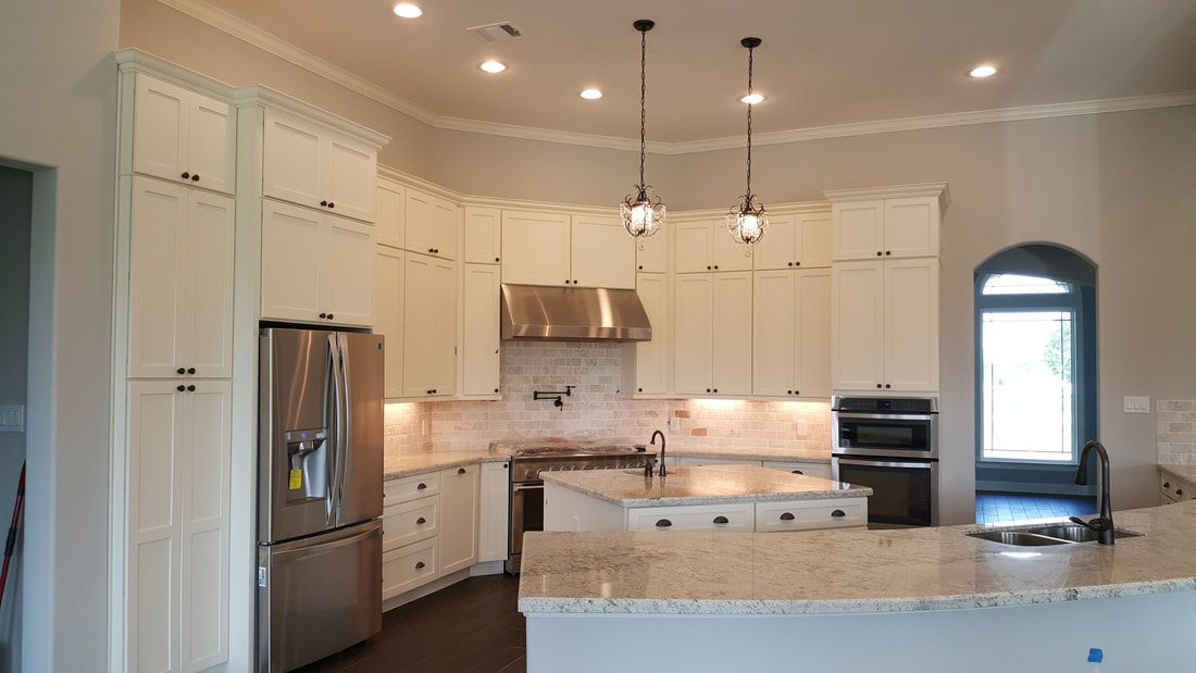 Bright white kitchen with stainless steel appliances, stone countertops, and hanging pendant lights.