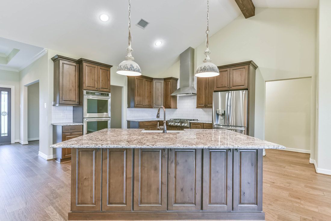 Kitchen with island, brown cabinets, stainless steel appliances, and hanging lights.