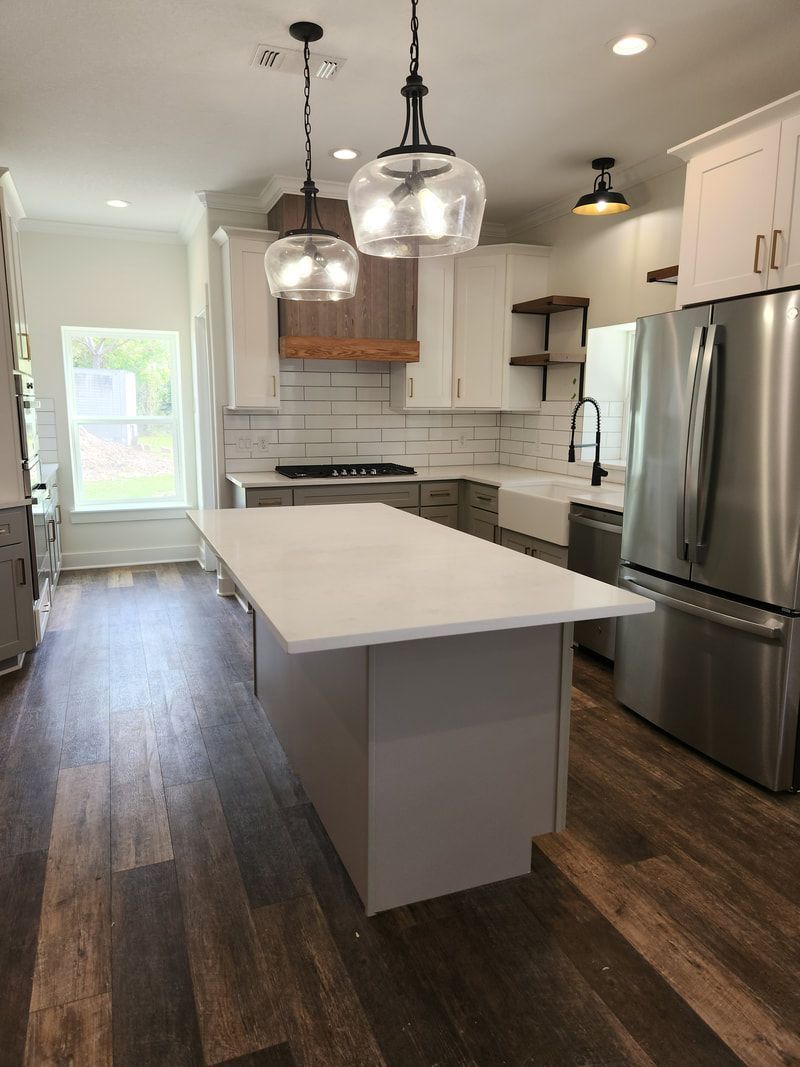 Modern kitchen with white cabinets, island, stainless steel appliances, and wood flooring.
