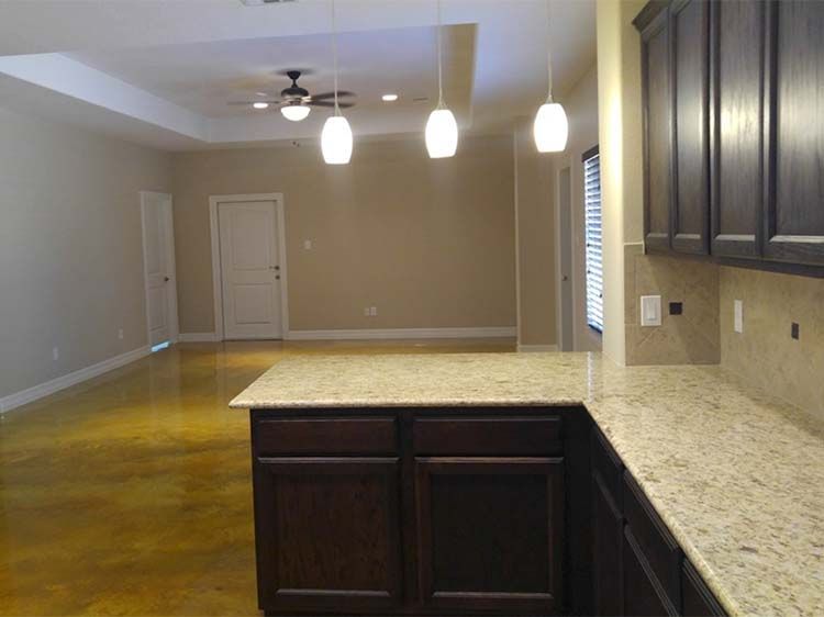 Kitchen with dark wood cabinets, light countertops, and beige walls, leading to a living area with a door.