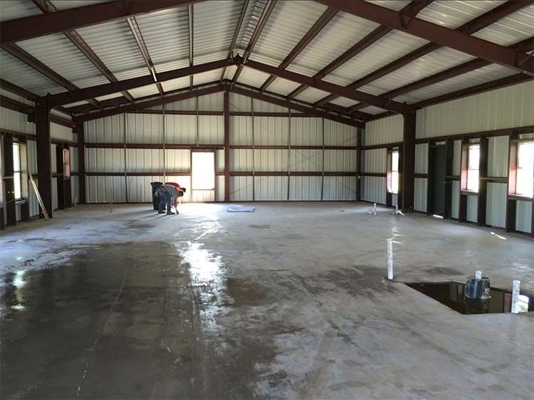 Interior view of a large, empty metal building with a wet concrete floor and steel support beams.