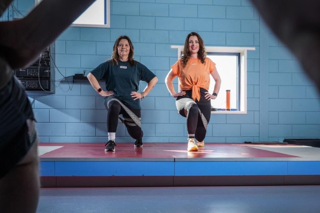 Twee vrouwen in fitnesskleding doen lunges met weerstandsbanden in een sportschool.