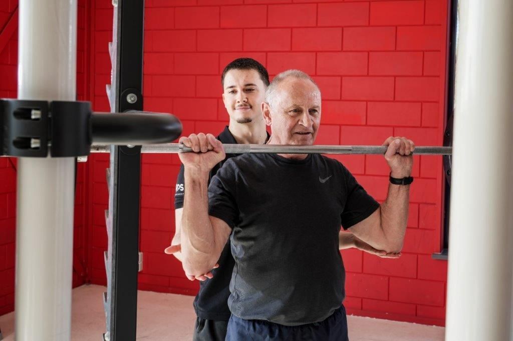 Man doet squats met een hometrainer. Rode bakstenen muur.