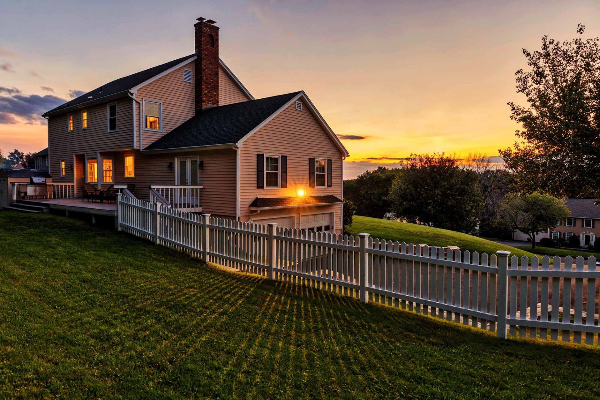 beautiful country house with white fence, green lawn, and sunset on background