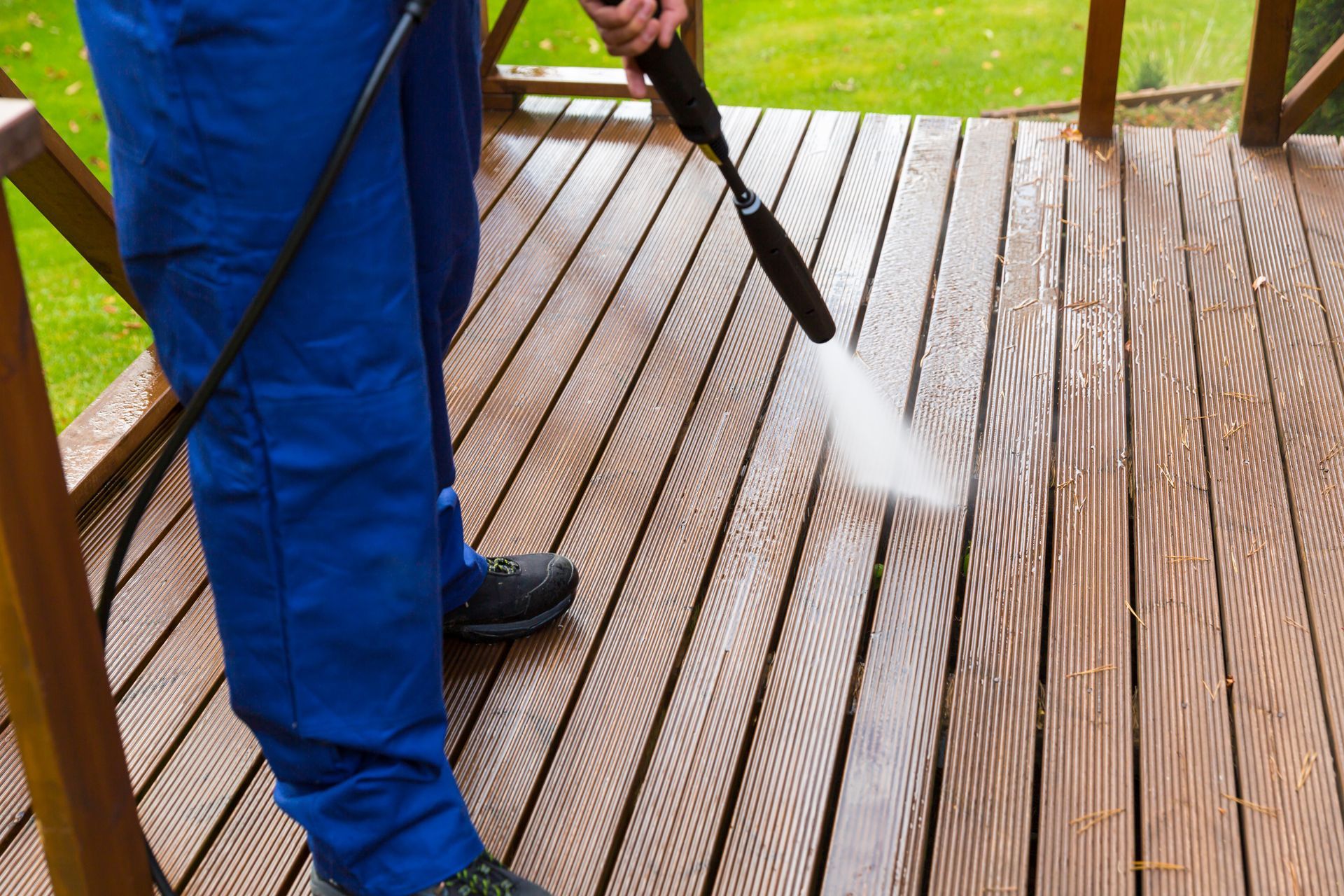 A person using a high-pressure washer to clean a wooden terrace.