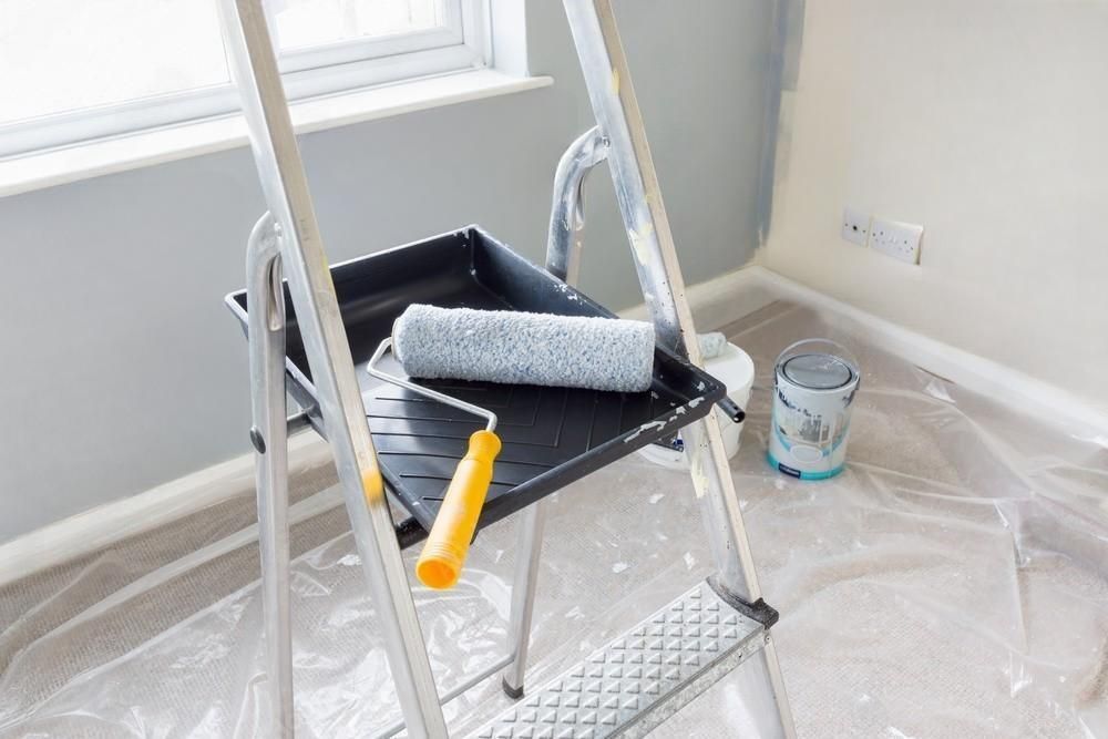 A ladder with a paint roller and tray on it in a room.