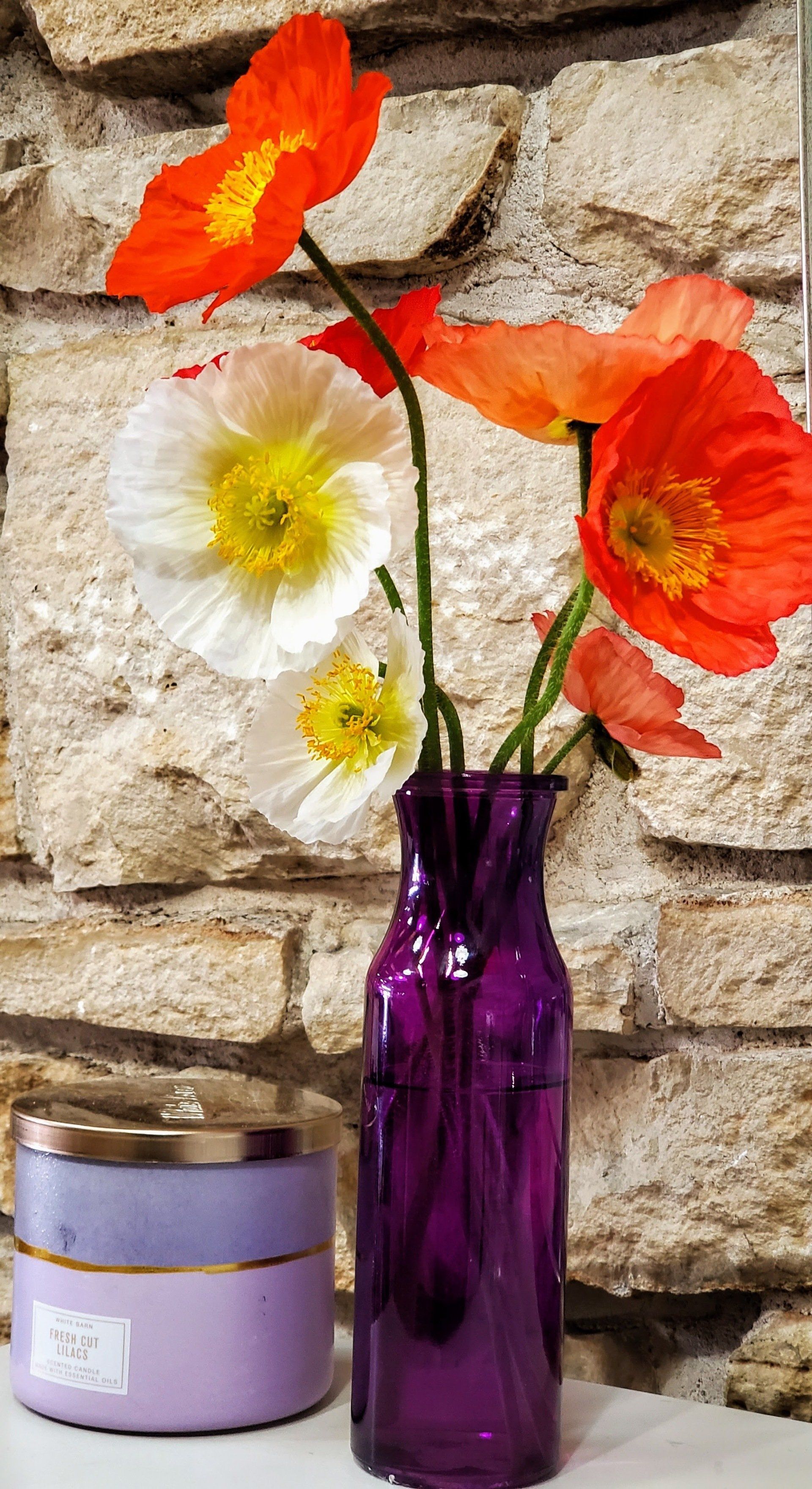 A vase filled with flowers is sitting on a table in front of a stone wall.