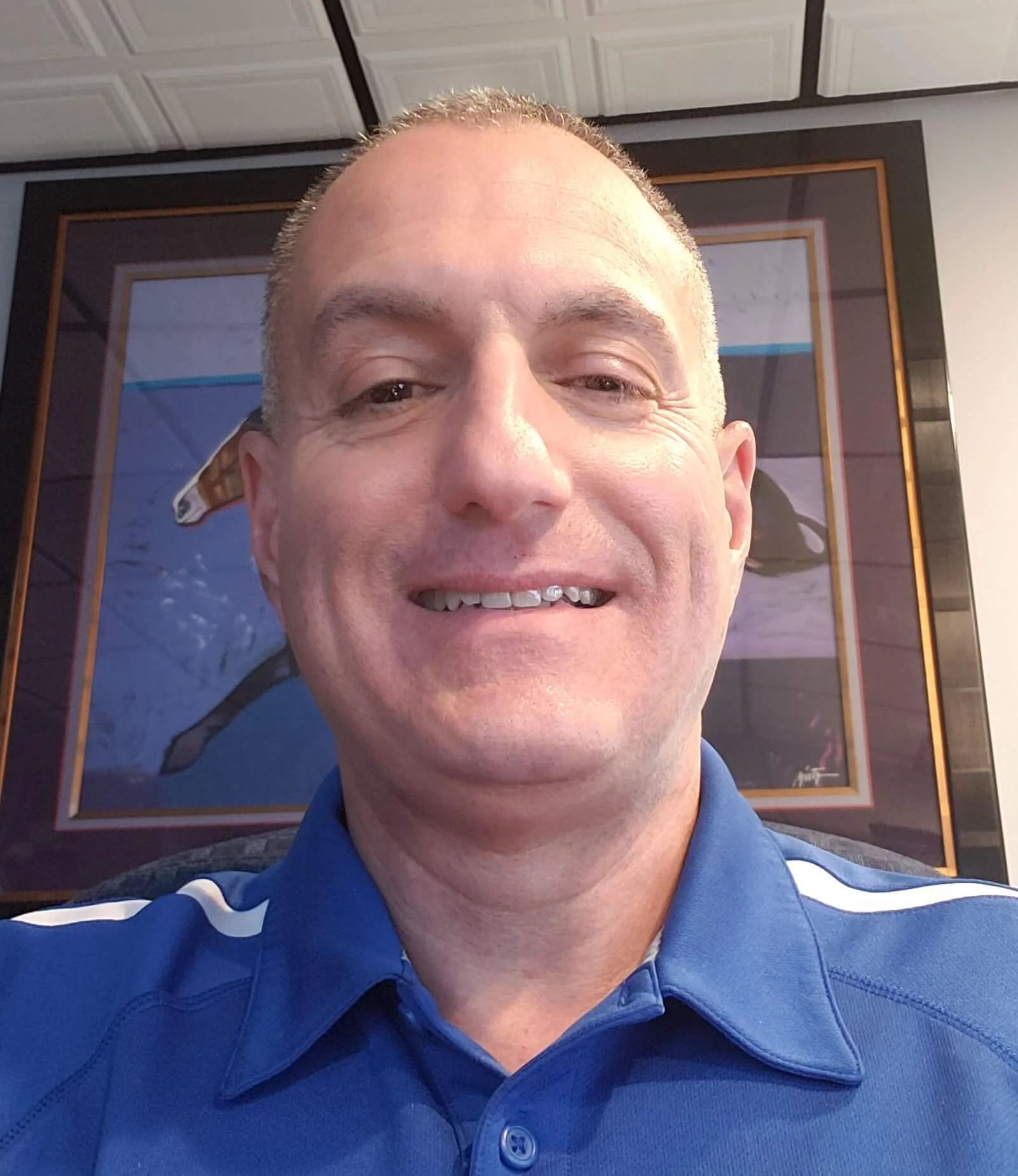 Man smiling, wearing a blue collared shirt; horse artwork in the background.