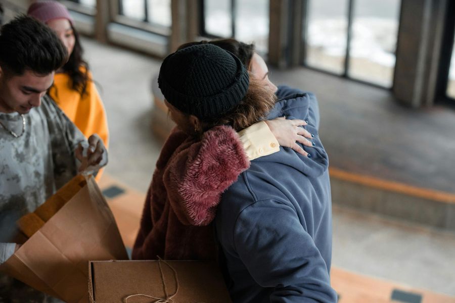 People hugging in an entryway, with boxes and others watching.