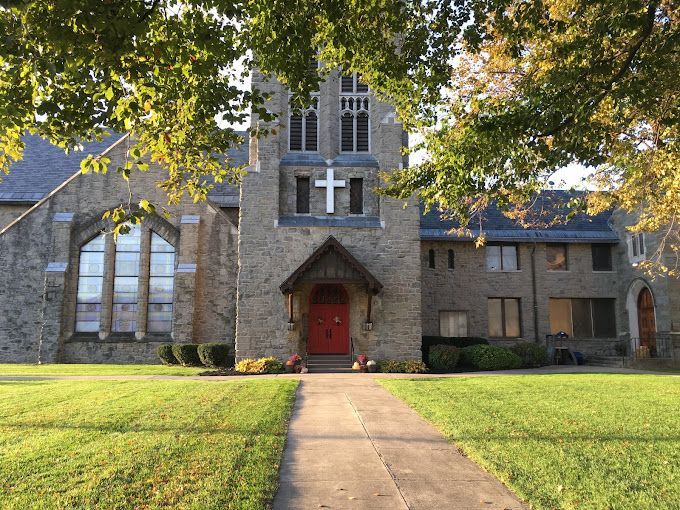 Stone church with a red door, white cross, and stained-glass window. Path leads to the entrance.