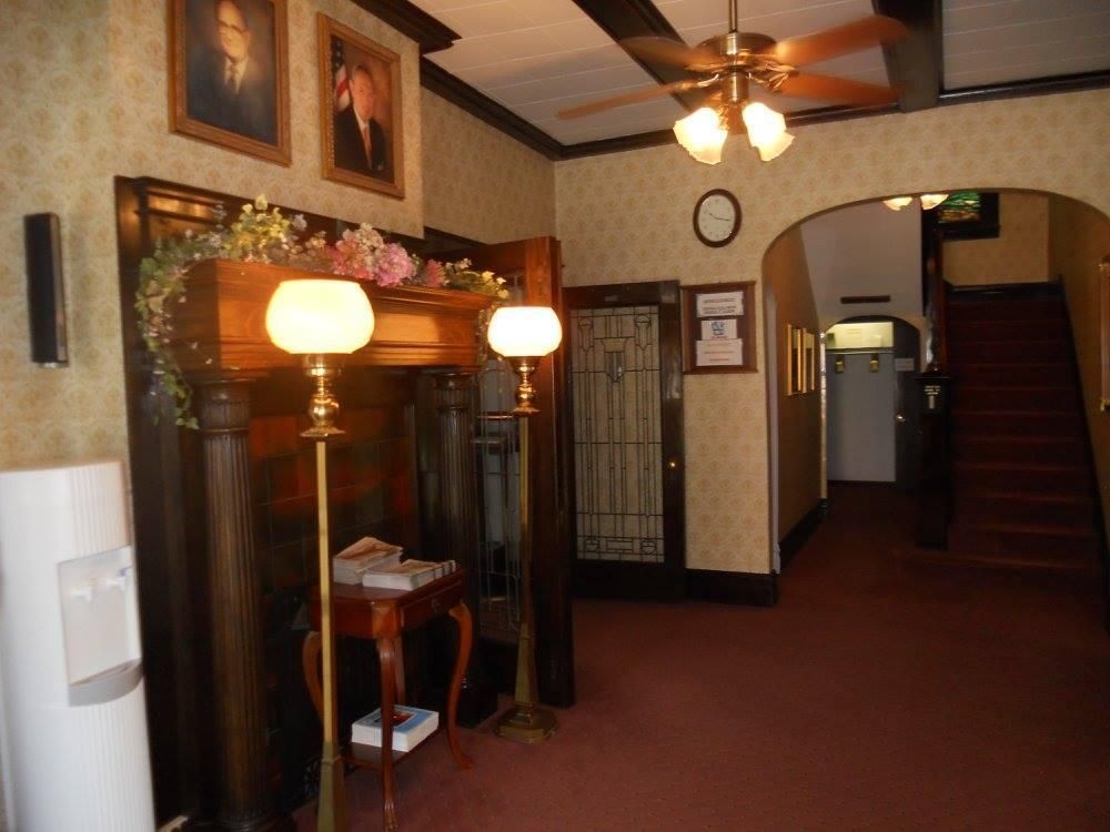 Hallway with dark wood paneling, floral wallpaper, portraits, and a staircase.