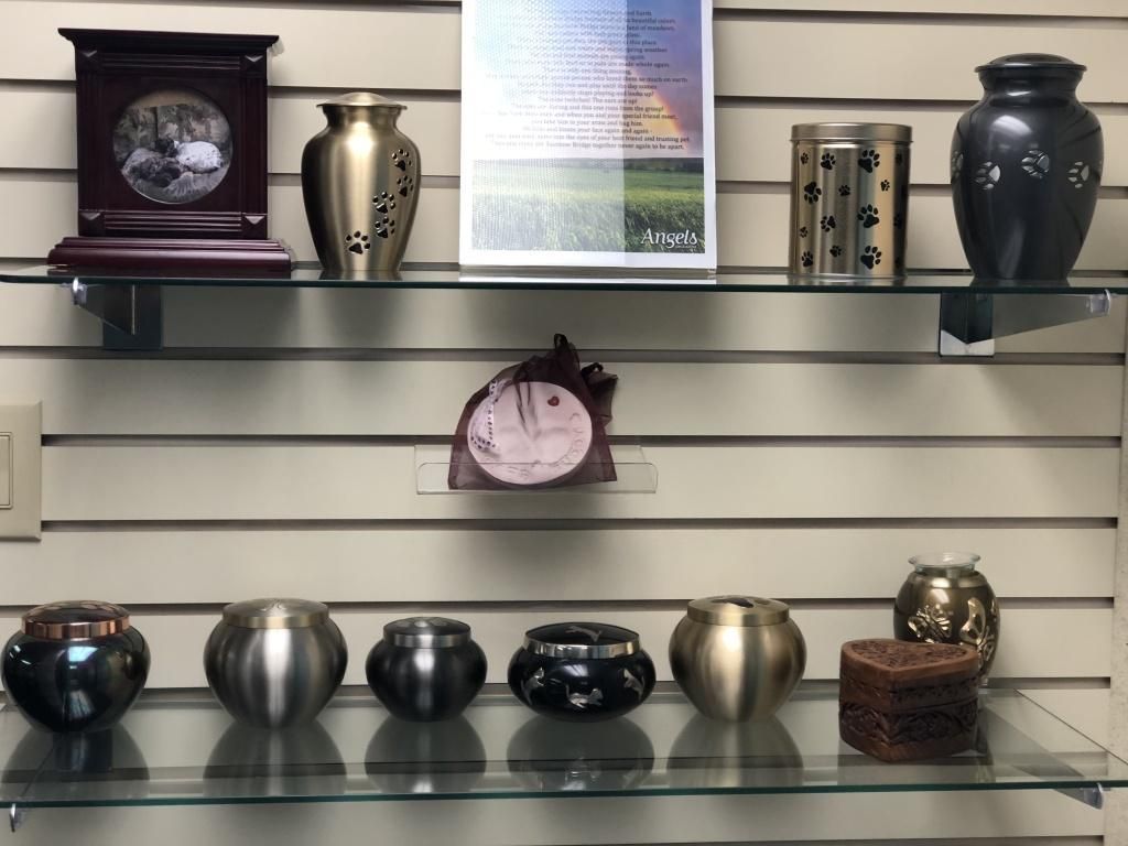 Shelves displaying pet cremation urns in various styles and colors against a slatted wall.