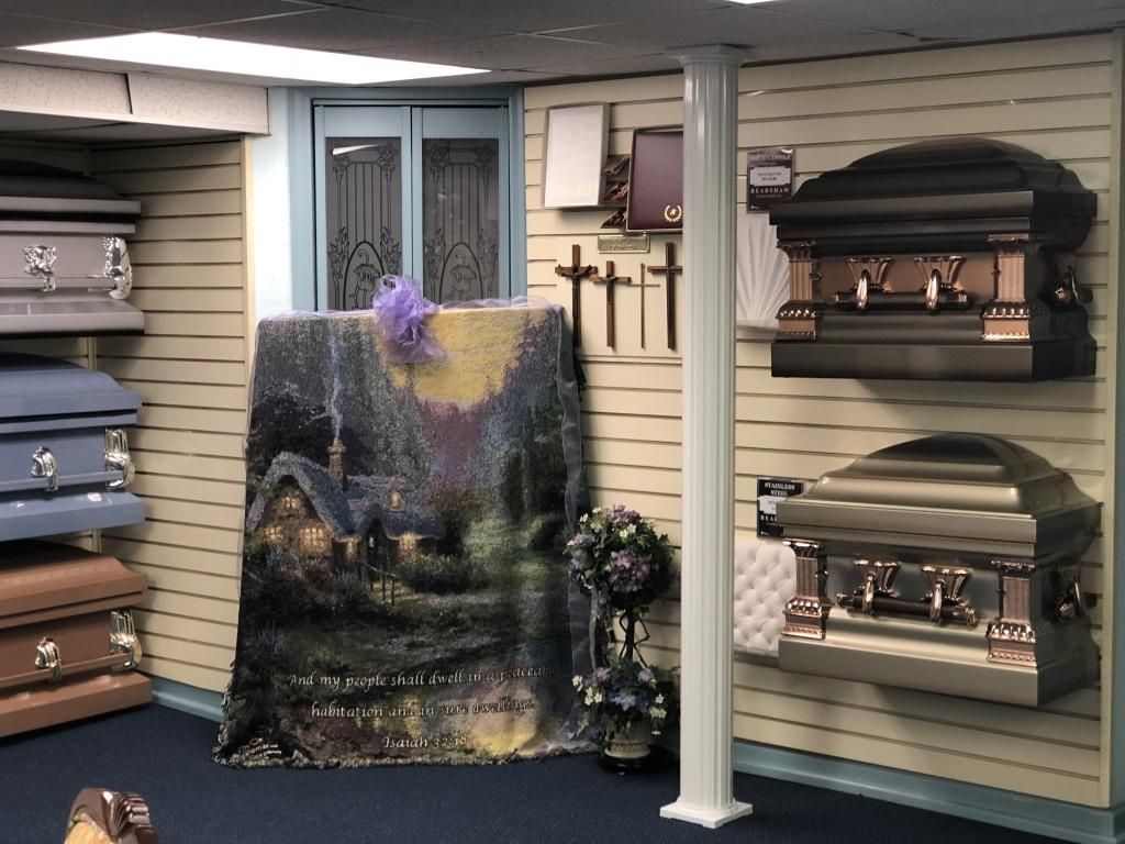 Display room in a funeral home; caskets line walls, artwork displayed.